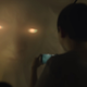 A boy holding a camera phone stares a giant, menacing face with glowing eyes.